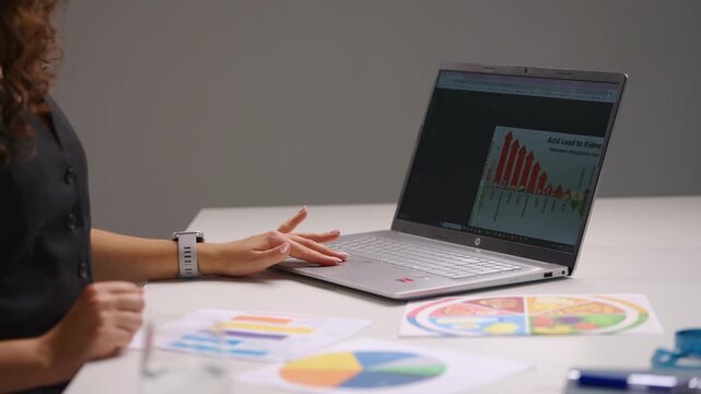 Close view of a woman working at a desk, using a tablet to zoom into charts and diagrams on a laptop screen, showing technology, data analysis, business planning and modern professional workflow