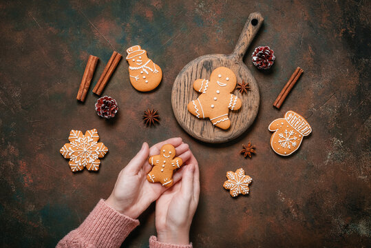 Female hands holding gingerbread man on dark grunge table, Christmas various gingerbread cookies, top view, flat lay.