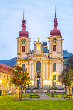 The former Franciscan monastery and pilgrimage Church of the Visitation are shown in the evening light. The buildings stand tall in Hejnice with a backdrop of mountains.