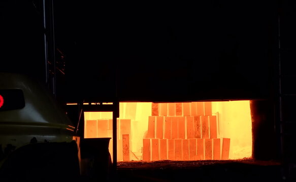 A high-temperature furnace glows bright orange, revealing neatly arranged refractory blocks inside. The intense illumination highlights the heat-resistant materials used for thermal processing in heav