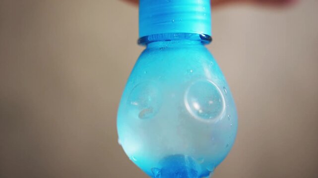 Macro of inverted blue plastic bottle base as frost and condensation spread