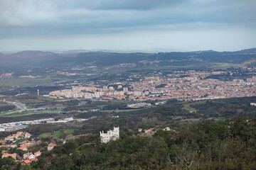 Obraz premium A stunning panoramic scene captures an expansive town nestled in the valley, framed by rolling hills and dramatic clouds, showcasing nature's grandeur juxtaposed with urban life