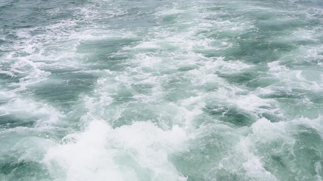 White churning foam and bubbles in the turquoise water trail behind a moving vessel. Turbulent ocean waves and splash texture background. Professional shot of a ship wake in the open sea.