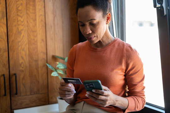 Mature woman using a credit card and smartphone at home for mobile banking, online payment and personal finance management