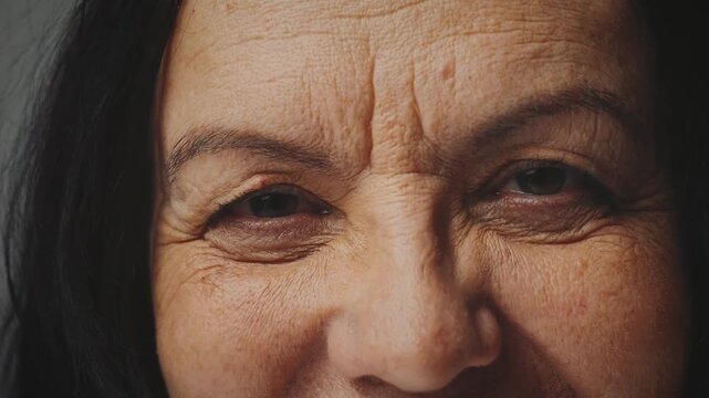 close-up brown eyes sight senior elderly mature woman looking at camera. business lady in office old age skin with deep wrinkles. joy positive mood, beauty happy woman smiling eye part of face cut off