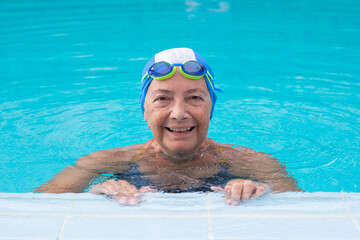 Fototapeta premium Happy senior woman enjoying a refreshing swim in a bright blue pool, wearing a swim cap and goggles, actively engaging in a healthy, active lifestyle and wellness