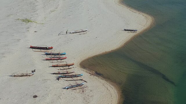 Aerial view of traditional wooden outrigger boats resting on the sandy beach of Morondava, with calm coastal waters and clear shoreline in Morondava, Menabe, Madagascar.