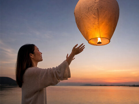 Young woman releasing a glowing sky lantern at sunset over water