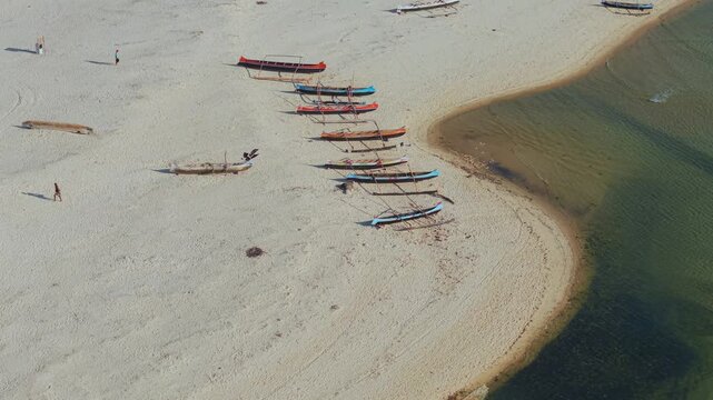 Aerial view of traditional wooden outrigger boats resting on the white sandy beach with people walking nearby in Morondava, Menabe, Madagascar.