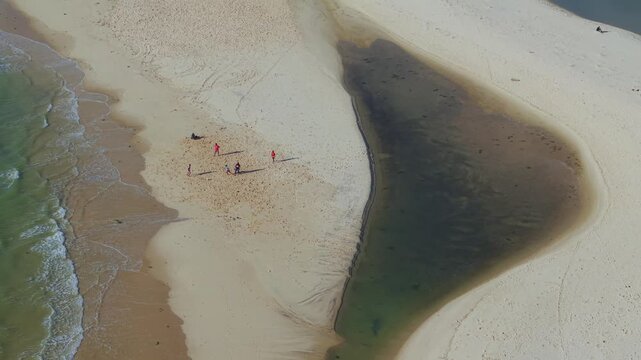 Aerial view of a sandy beach with a small water inlet and people walking along the shore in Morondava, Menabe, Madagascar.