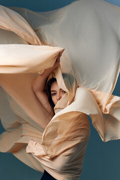 Woman playfully wrapped in billowing cream fabric with sculptural movement. Concept of beauty branding, bridal ads and fashion editorial.