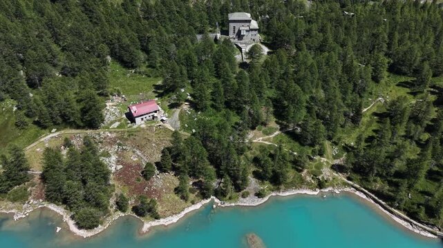 Aerial view of the Palu Hydroelectric Power Plant nestled among dense pine forests and alpine terrain above the turquoise waters of the lake in Poschiavo, Grisons, Switzerland.
