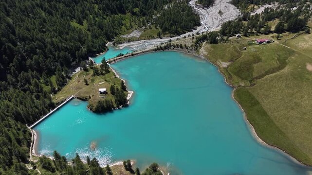 Aerial view of the turquoise waters of Lago di Palu and the Wasserkraftwerk Palu dam surrounded by alpine forests and mountains in Poschiavo, Grisons, Switzerland.