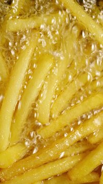French Fries Frying in Hot Oil. Macro view of golden potato fries bubbling and sizzling during deep frying.
