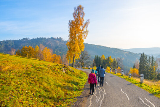 People walk along a road surrounded by autumn trees in Albrechtice, located in the Jizera Mountains, Czechia. The colorful leaves mark the change of the seasons.