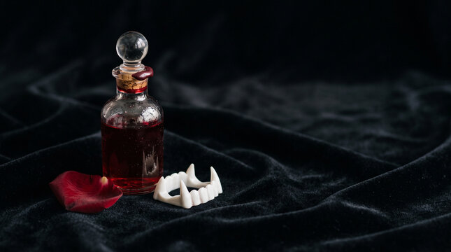 Glass vial with red liquid and decorative fangs on black fabric  