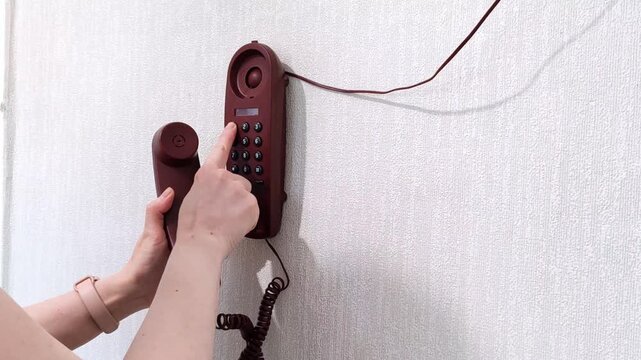 Female hands holding a wall phone receiver and dialing 911 emergency number on the keypad. Closeup action shot of a person calling for help, rescue service and crisis situation.
