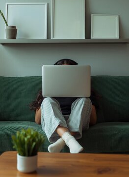 Anonymous woman working on laptop covering face sitting on green sofa at home
