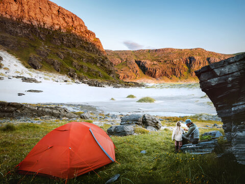 Father and child on camping vacation travel in northern Norway with tent outdoor gear, family adventure hiking tour parent and kid enjoying sunset mountains view in Finnmark