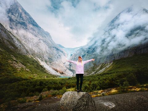 Woman hiking mountains in Norway travel solo active vacations tourist raised hands enjoying Briksdalsbreen glacier view, healthy lifestyle summer holidays retreat tour in Stryn, harmony with nature