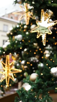 Close up vertical shot of a beautiful golden shining star topper and elegant bauble hanging on a green Christmas tree branch with warm festive lights.