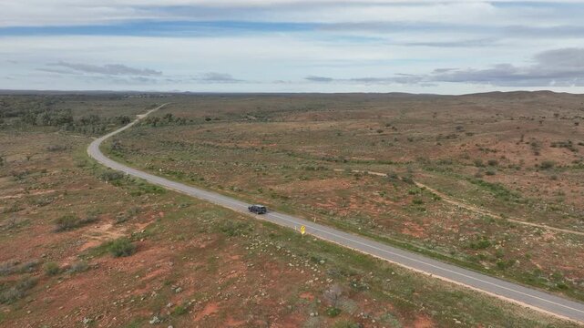 Cinematic aerial tracking shot following a vehicle along a winding road through the rugged red-earth outback near Silverton and Broken Hill, New South Wales.