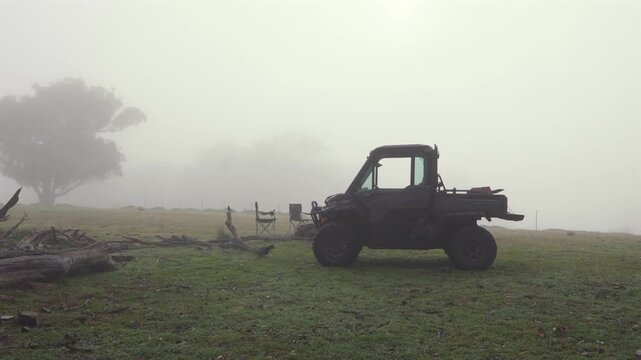 Moving gimbal shot revealing a rugged utility vehicle parked on a grassy paddock surrounded by dense fog in the Southern Highlands countryside of New South Wales, Australia.