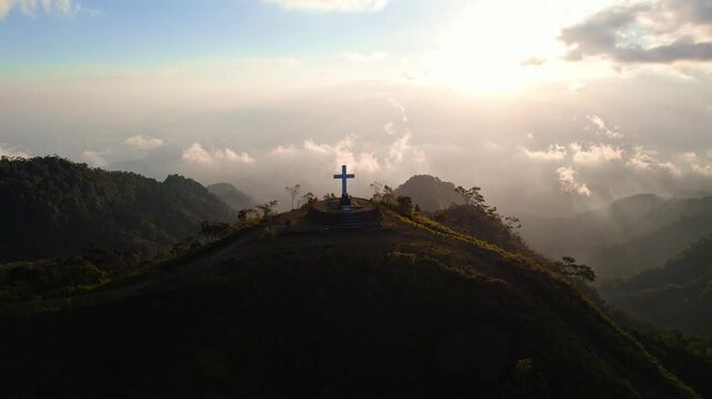 Aerial view of the Wolo Ata Ga'e Statue atop a mountain peak surrounded by clouds during golden hour in Bajawa, Nusa Tenggara Timur, Indonesia.