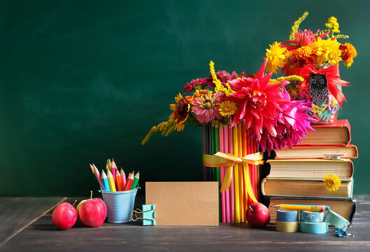 Education, back to school, beginning of the school year, Teacher's day, Knowledge Day, 1 September concept. Stack of books, school stationery, apples, flowers bouquet on table against chalkboard