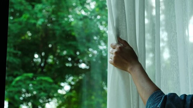 woman's hand She opened the curtains on the window. There was morning light through the window in her room, looking at the view of the mountains and trees as the sun rose	