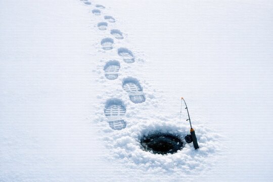 A fishing pole stuck out of a hole in the snowy ground, great for winter or outdoors scenes