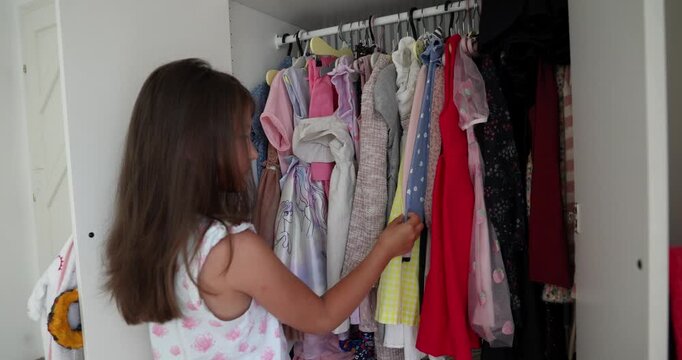 Little girl choosing clothes from the wardrobe. Girl choosing dress a lot of clothes in the child wardrobe