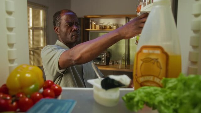 Senior African American man opening refrigerator, smelling expired yogurt with disgusted face, and putting it back. Video is perfect for food safety or healthy eating advertisements