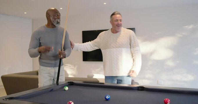 Diverse men at pool table watching senior man striking cue, scattering balls, playing, cheering