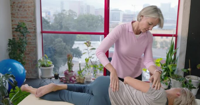 Female therapist in pink placing, checking and mobilizing senior on padded table aligning