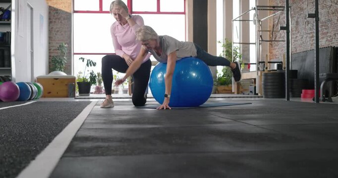 On trainer cue, senior woman doing arm-leg extensions on blue stability ball in gym for stability