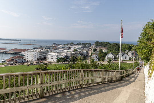 View of the historic town and harbor of Mackinac Island with lush greenery, a wooden fence, and an American flag under a clear blue sky in Mackinac Island, Michigan, United States.