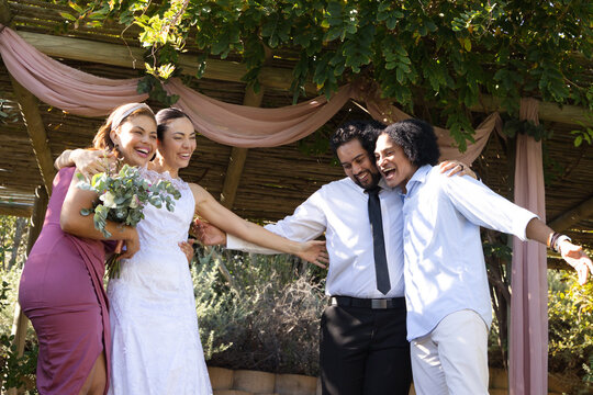 Diverse wedding party wearing bridal gown mauve dress and tie under pergola holding bouquet