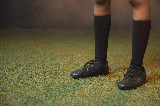 Woman standing on turf at studio wearing black knee-high socks and untied soccer shoes, copy space