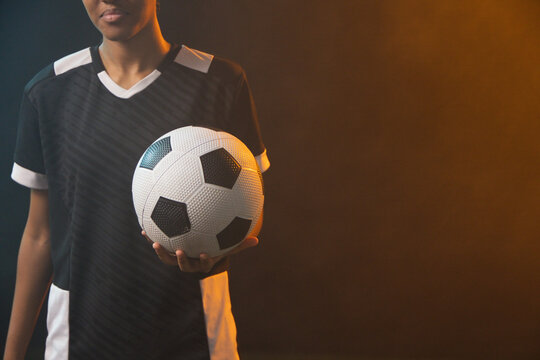 African American woman standing left in studio, in black jersey holding soccer ball, copy space