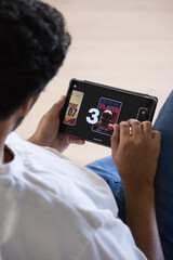 African American man on sofa holding tablet, playing game showing 3 and ZONE 07, copy space © wavebreak3