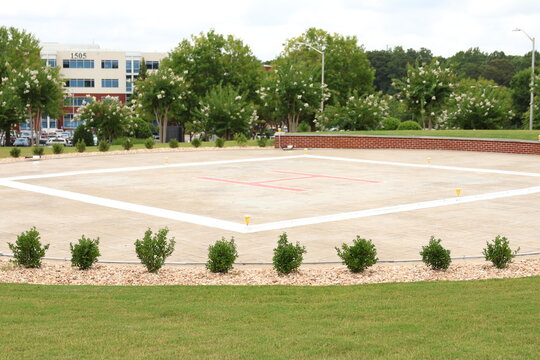 Empty outdoor helipad landing pad surrounded by green trees and buildings.