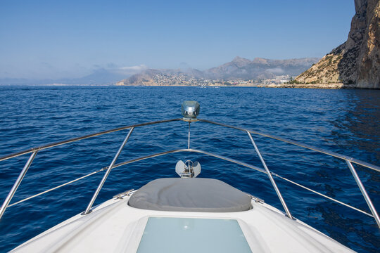 View of the Mediterranean Sea from the bow of a boat, with the Penon de Ifach and the coastal town of Calp in the distance under a clear blue sky, Calp, Comunidad Valenciana, Spain.