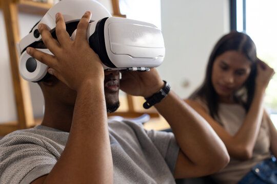 African American couple sitting on couch, man adjusting white VR headset, wearing gray shirt