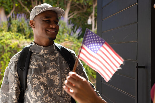 African American man standing at porch in camo uniform with backpack accepting hand-held US flag