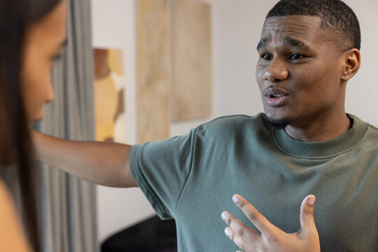 Diverse adults conversing, man gesturing, wearing green crewneck tee, curtain, art, sofa at home