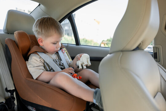 Toddler boy safely secured in child car seat playing with toy during family road trip