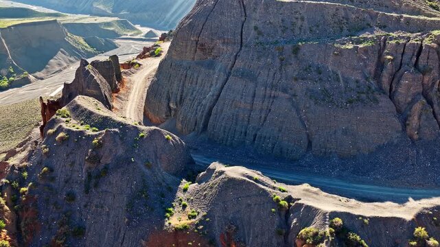 Aerial view of a narrow dirt road winding along steep canyon cliffs and mountain ridges in Anjihai Grand Canyon, Xinjiang, China