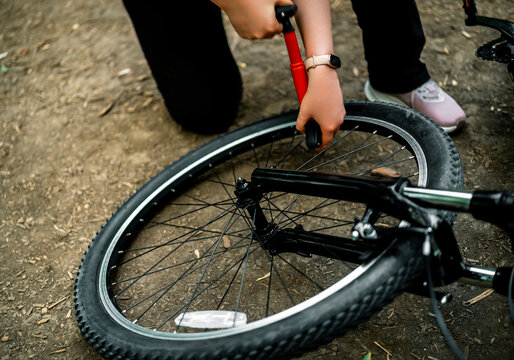 Hands of cyclist inflating bicycle tire with red hand pump on dirt road. Outdoor sports equipment maintenance and active travel concept