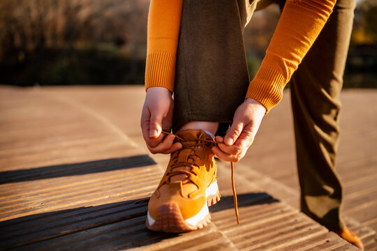 Woman hands on shoelaces of brown hiking boots at wooden path Concept of preparation active outdoor lifestyle autumn journey